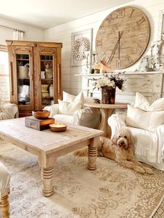 a living room with white couches and a wooden table in front of a large clock