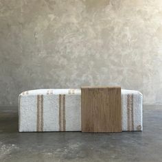 a wooden block sitting on top of a white and brown striped bench in front of a wall