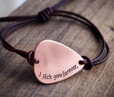 a leather cord bracelet with a copper heart and i pick you forever engraved on it