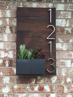 a house number sign mounted to the side of a brick wall with succulents in it