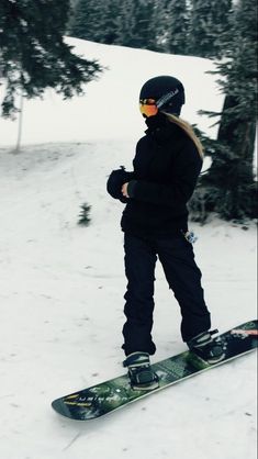 a person riding a snowboard on top of a snow covered slope with trees in the background