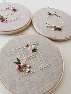 three embroidered hoops with flowers and the letter e on them are sitting next to each other