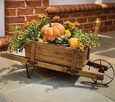 a wooden wagon filled with flowers and pumpkins on the side of a brick building