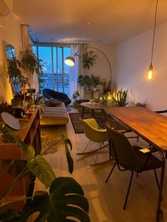 a living room filled with lots of furniture and plants on top of wooden flooring