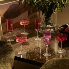 a table topped with lots of wine glasses next to a vase filled with fruit and vegetables