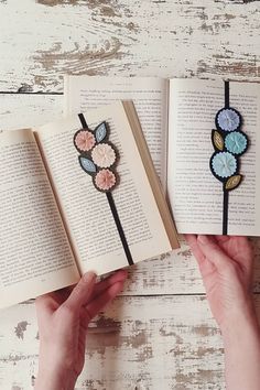 two bookmarks with flowers on them are being held in front of an open book