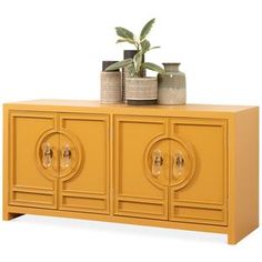 a yellow cabinet with three doors and two vases on the top one has a plant in it