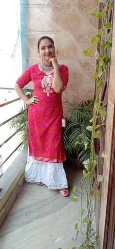 a woman standing on a balcony talking on a cell phone and wearing a pink dress