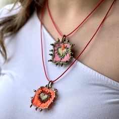 a woman wearing a necklace with two pendants on it's sides and an orange flower in the center