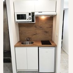 a small kitchen with white cabinets and wooden counter tops, including a microwave above the sink