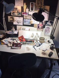 an office desk with many items on it and a lamp over the top that is turned on