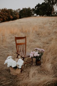 a wooden chair sitting on top of a dry grass field next to a basket filled with flowers