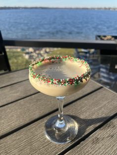 a drink sitting on top of a wooden table next to the ocean with sprinkles