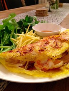 a white plate topped with an omelet covered in cheese and shrimp next to greens