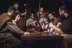 a group of men sitting around a wooden table with shields and spears on their heads