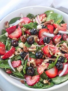 someone pouring dressing onto a salad with strawberries and spinach