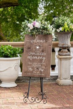 a welcome sign with flowers on it in front of some potted plants