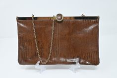 Gorgeous classic brown clutch made out of an alligator leather-like material. It has clasp on the top that flips up to open. The bag itself has a double hinged opening to give you full access to all the little goodies hiding at the bottom of your bag! It is fully lined and ready to be taken out on the town.   Good, vintage condition. Some tarnishing / wear on the back of the gold cap at the top. Measurements: 11 W x  6.5" H x .5" D 18.5" drop at strap Please reach out with any questions prior to Elegant Brown Clutch With Fold Over Clasp, Brown Rectangular Clutch With Fold Over Clasp, Brown Evening Bag With Chain Strap, Brown Crocodile Pattern Evening Shoulder Bag, Evening Brown Crocodile Pattern Shoulder Bag, Formal Brown Rectangular Clutch, Formal Brown Evening Bag With Chain Strap, Brown Clutch, Gold Cap