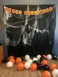 halloween decorations and balloons on the floor in front of a black backdrop with happy halloween written across it