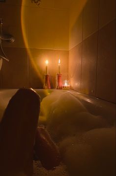 a person laying in a bathtub with candles on the side