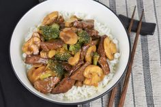 a white bowl filled with beef and broccoli on top of rice next to chopsticks