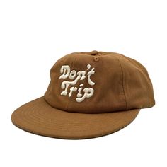 On a white background is a brown unstructured 6 panel baseball hat with white embroidery that reads, Don't Trip. Cotton Snapback Hat For The Beach, Cotton Snapback Trucker Hat For Vacation, Adjustable Cotton Snapback Hat For Beach, Retro Short Brim Travel Hat, Retro Short Brim Hat For Travel, Brown Retro Hat For Outdoor, Cotton Trucker Hat For Vacation, Cotton Trucker Hat With Flat Bill For Beach, Vintage Cotton Trucker Hat For Beach