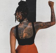 a woman with tattoos on her back standing next to a wall