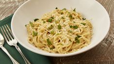 a white bowl filled with pasta on top of a green place mat next to silverware