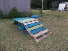 an upside down wooden bench in the grass next to a shed and yard with a blue wheelbarrow