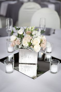 a centerpiece with white flowers and candles on a silver tray at a wedding reception