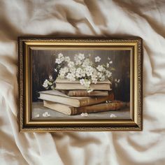 an oil painting of books and flowers in a gold frame on a white bed sheet