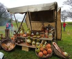 many pots and vases are on display in the grass near a tent with people standing around it