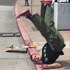 a young man is doing a handstand on the sidewalk with his skateboard