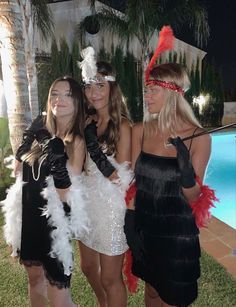 three women dressed in costumes standing next to each other near a swimming pool at night