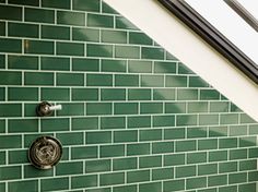 a green tiled wall with two faucets on each side and a window above it