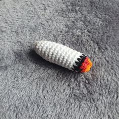 a crocheted carrot laying on top of a gray carpet with orange and black stripes