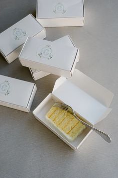 four pieces of cake sitting in small white boxes with spoons next to each other