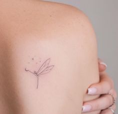 the back of a woman's shoulder with a small dragonfly tattoo on it