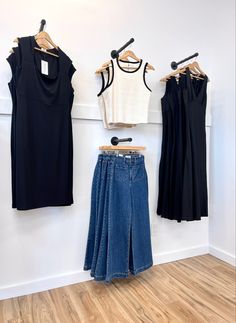 clothes hanging up against a wall in a clothing store with wooden flooring and white walls