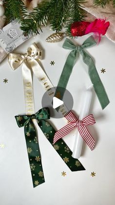 three christmas ribbons are tied together on a white surface next to evergreen branches and other holiday decorations