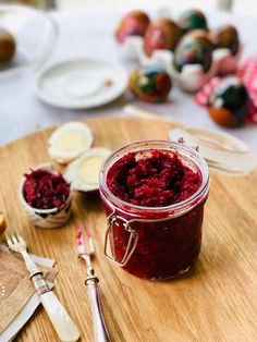 a wooden cutting board topped with a jar of beet jam next to other food