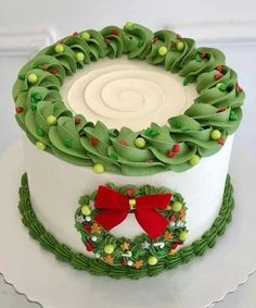 a white cake with green icing and red bow on top, decorated with holly wreaths