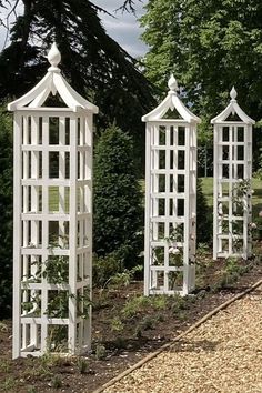 three white garden arbors sitting next to each other on a gravel path in front of trees