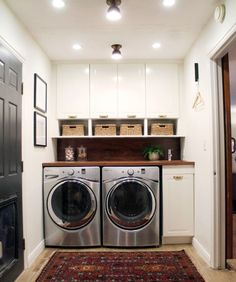 a washer and dryer in a small laundry room with white cabinets, rugs and baskets on the wall