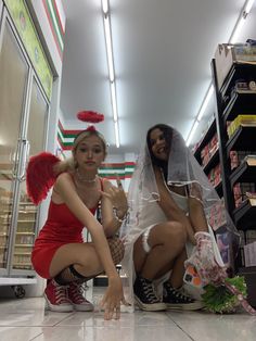 two women dressed up in costumes sitting on the floor next to each other at a store