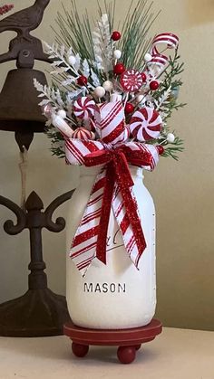 a mason jar filled with candy canes and greenery sits on a table next to a bell