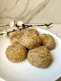 four sesame seed cookies on a white plate with flowers in front of it and marble background