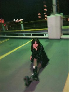 a woman riding a skateboard down a street next to a parking lot at night