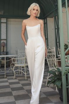 a woman standing on a checkered floor wearing a white jumpsuit with one shoulder