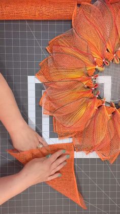 a woman is working on an orange flower decoration with scissors and fabric pieces to make it look like they have been made out of mesh